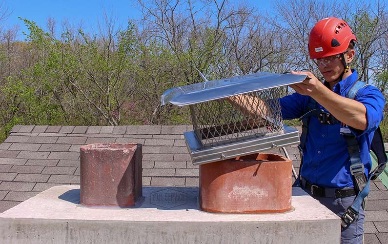 Technician installing a chimney cap on residential chimney