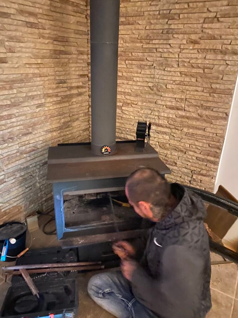 Technician cleaning a wood burning stove chimney from inside the home
