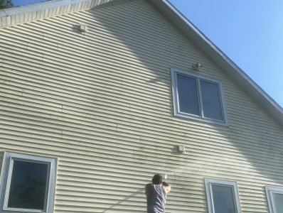 Technician pressure washing exterior siding of residential home