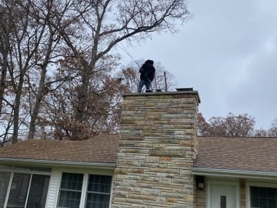Chimney technician cleaning a residential chimney from the roof